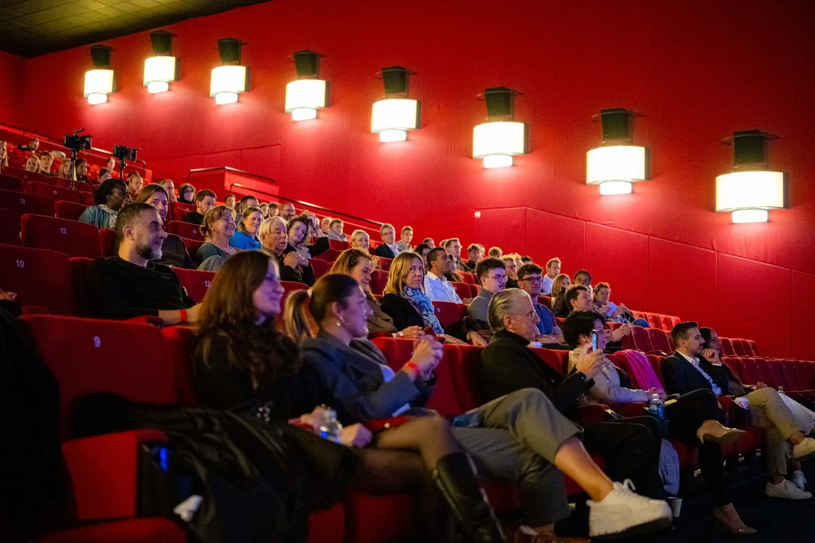 Audience in red seats under a row of warm lamps