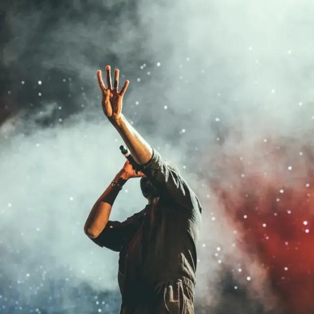 A performer on stage, arm raised, backlit by smoke and red light